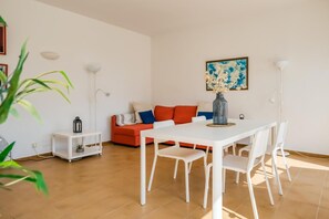 A modern living room with a white dining table, red sofa, and a painting on the wall. - Apartment "Orchidée"- sea view, swimming pool, air conditioning, terrace. (Es Mercadal)