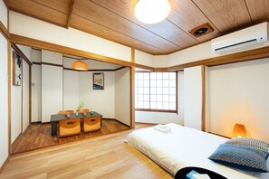 A room with a wooden ceiling, a bed with pillows, a bedside table, a window, and a dining area with a table and chairs. - TORA HOTEL Taito D (Tokyo)