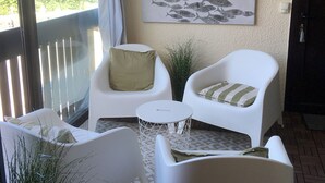 A balcony with white chairs, a small round table, and a potted plant.