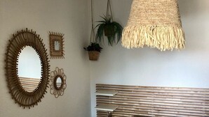 A bedroom with a bed, a hanging woven light fixture, two wall mirrors, and a potted plant.