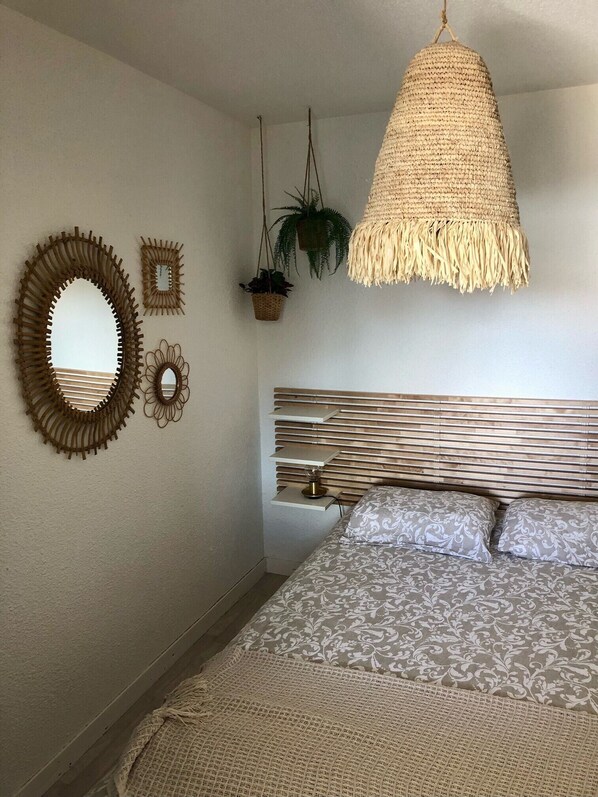 A bedroom with a bed, a hanging woven light fixture, two wall mirrors, and a potted plant.