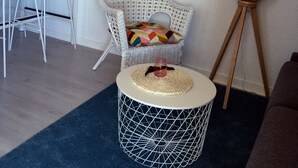 A living room with a round coffee table, a wicker chair, a white wicker sofa, and a dining area with white chairs and a small table.