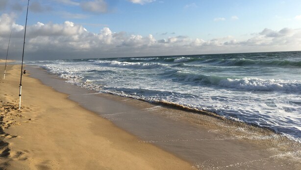 A beach with two fishing rods on the sand and waves crashing onto the shore.