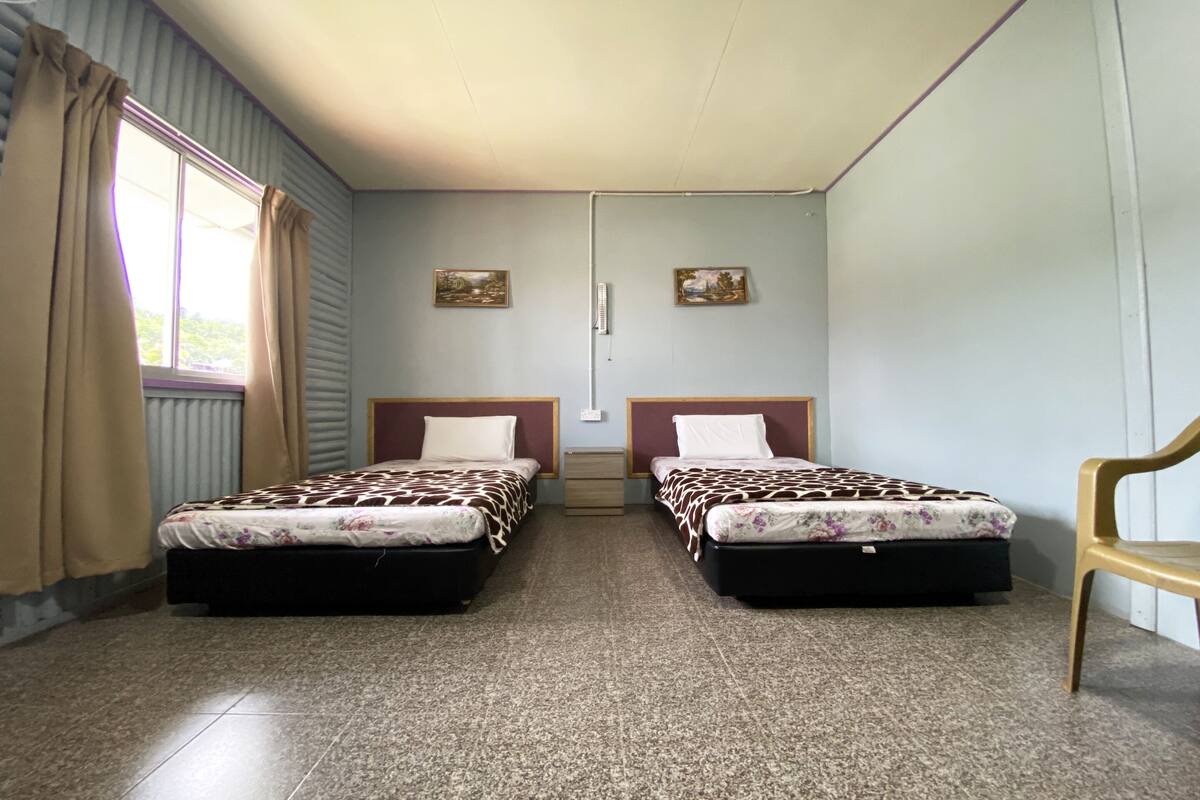 Een kamer met twee bedden, een raam met gordijnen, een radiator en twee foto's aan de muur.