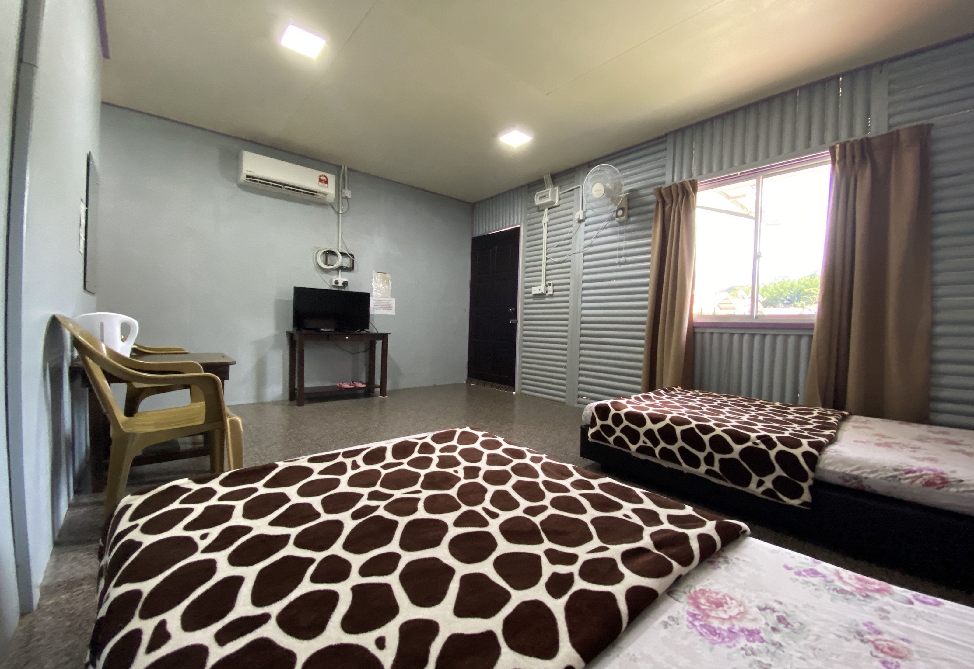 A hotel room with two beds, a television, an air conditioning unit, and a window with curtains.