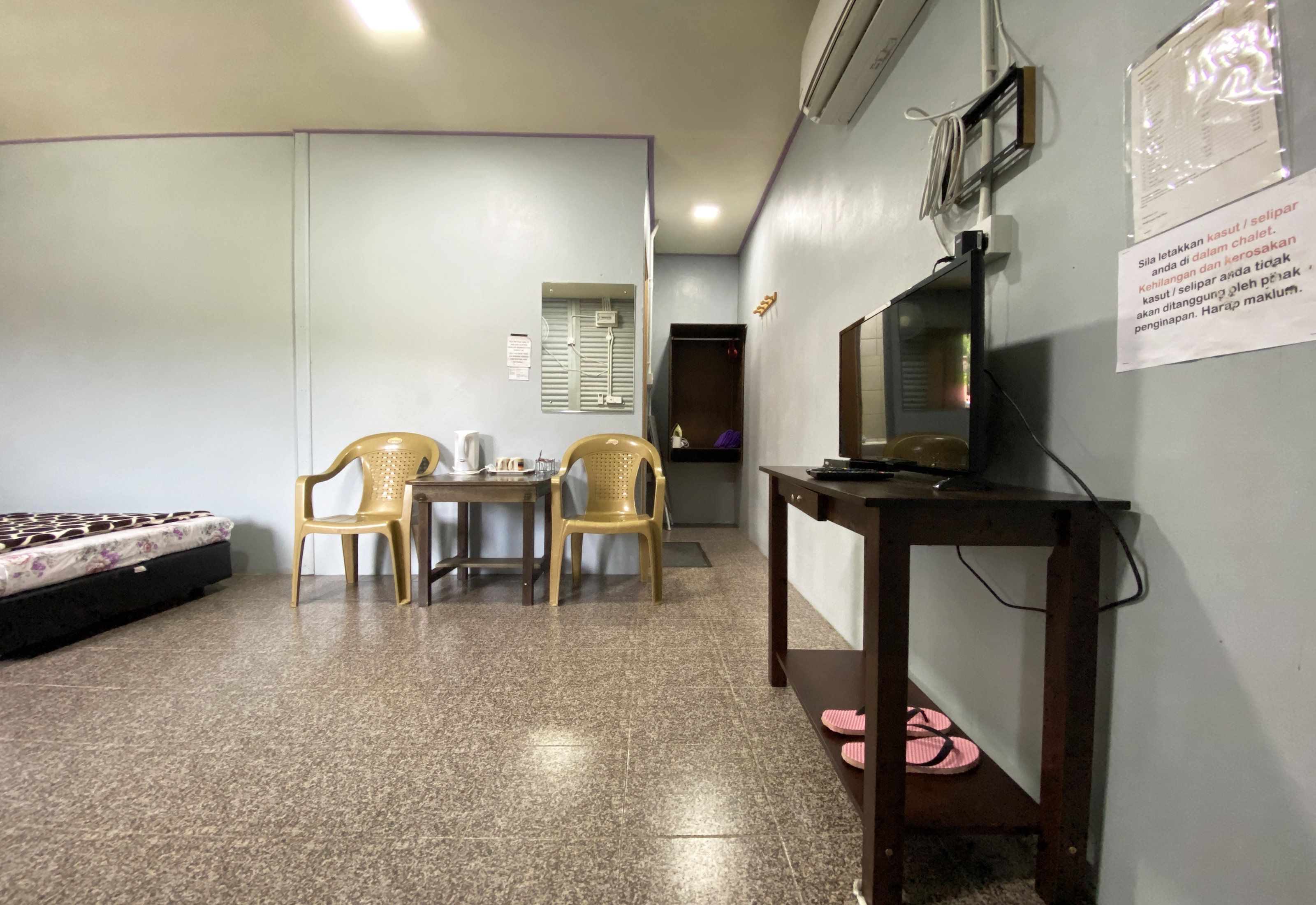 A room with a bed, a table with chairs, a television, and a wall-mounted air conditioner.