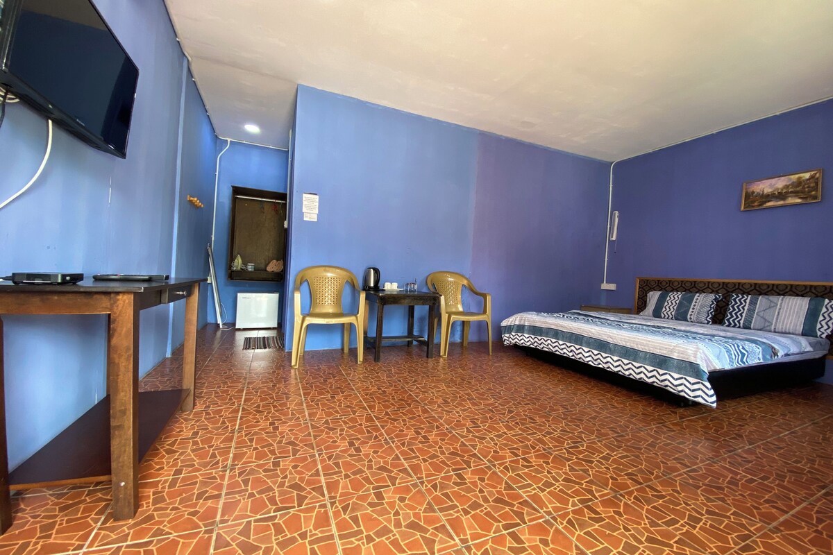 A room with a bed, two chairs, a small table, a television, and a tiled floor.