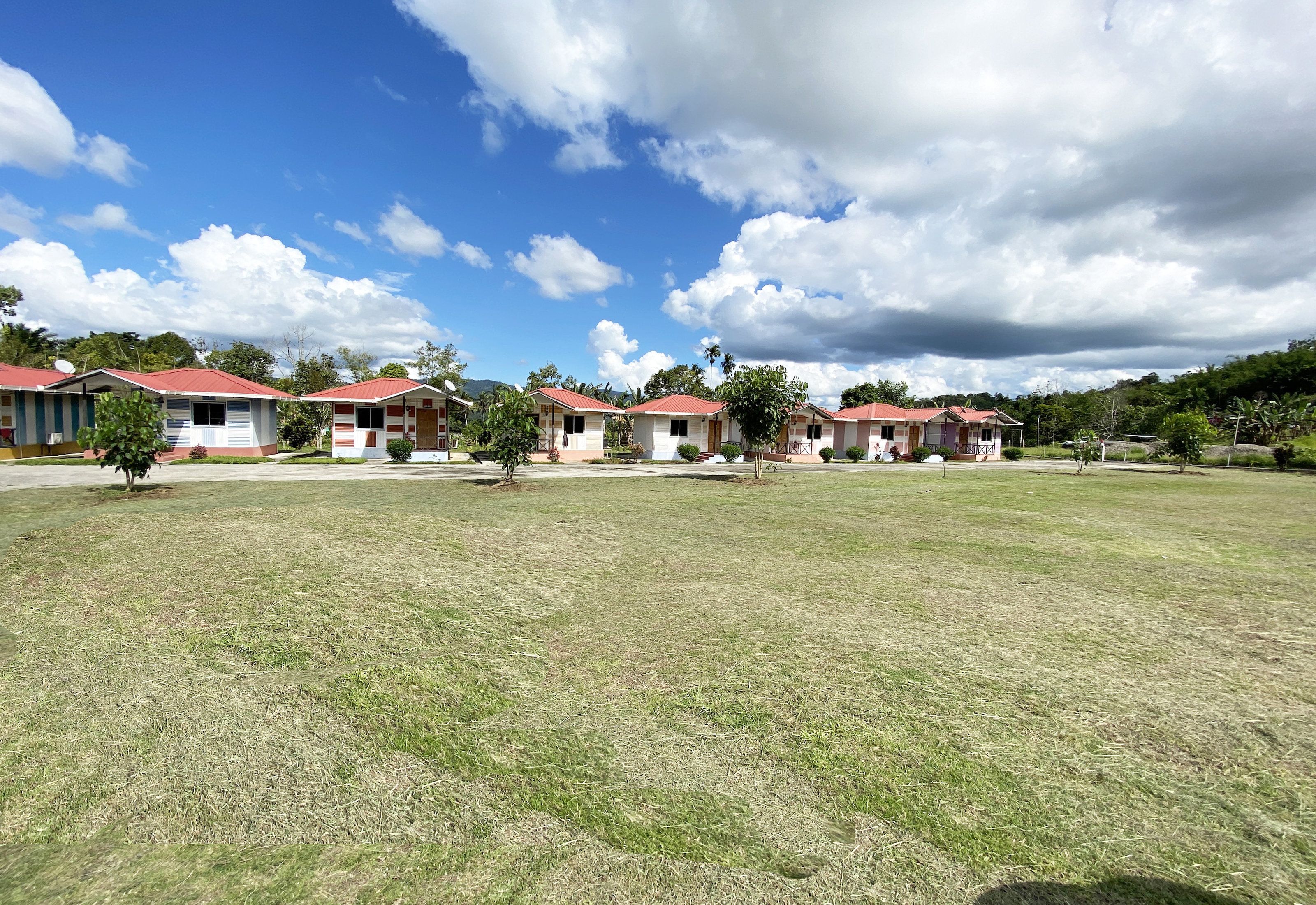 A row of single-story buildings with red roofs, surrounded by a grassy field and trees.