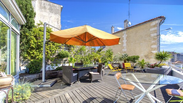 A wooden deck with outdoor furniture, including a glass table and chairs, and a large orange umbrella providing shade. - Maison 350 m Centre, Chambres Calmes, Spacieuses (Angoulême)