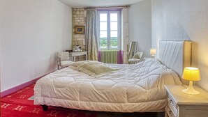 A bedroom with a bed, a nightstand, a lamp, a chair, a desk, a window with curtains, and a view of greenery outside. - Maison 350 m Centre, Chambres Calmes, Spacieuses (Angoulême)