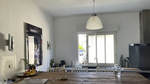 Ett kök med en köksö i trä, vita stolar, en hängande lampa och utsikt genom fönstret.