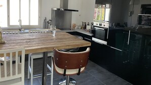 Ett modernt kök med ett träbord, vita stolar, en rostfri köksfläkt och svarta skåp.