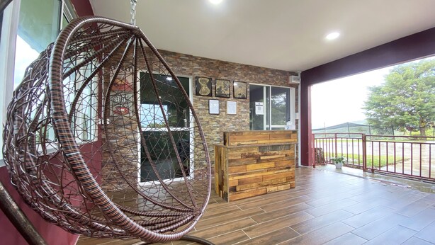 A wicker hanging chair, a wooden reception desk, and a view of the outdoors through a large window. - Hotel O Pogimpaan Homestay (Ranau)