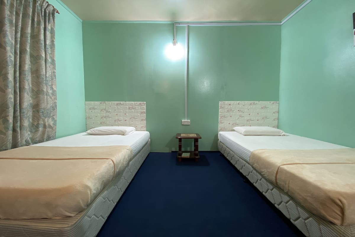 Una habitación con dos camas, una mesita de noche de madera y una lámpara en el techo.