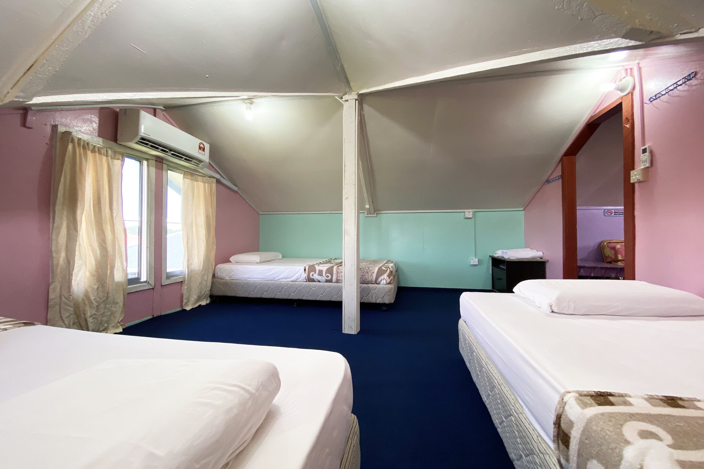 Una habitación con dos camas, una ventana con cortinas, un aire acondicionado y una mesita.