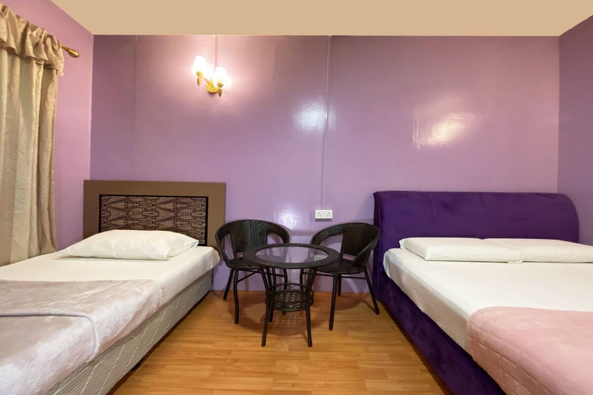 Una habitación con dos camas individuales, una mesa redonda con sillas y una lámpara fijada a la pared.