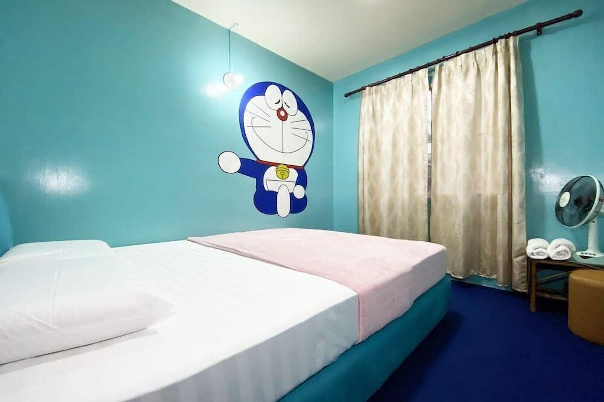 Una habitación con cama, ventilador de pared y ventana con cortinas.
