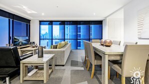 Una habitación de hotel moderna con vista a la ciudad, un comedor y una zona de estar con sofá y sillones.