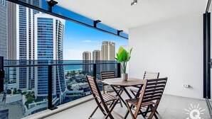 A balcony with a city view, a table with chairs, and a potted plant. - Circle on Cavill – 1 Bedroom Unit with Ocean Views (Surfers Paradise)