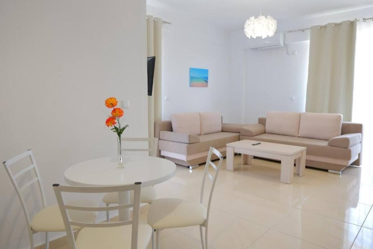 Een moderne woonkamer met een ronde eettafel, witte stoelen, een beige bank en een witte salontafel.