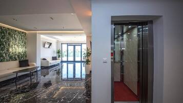 A modern lobby with a marble floor, a sofa, a coffee table, and a large abstract painting on the wall.