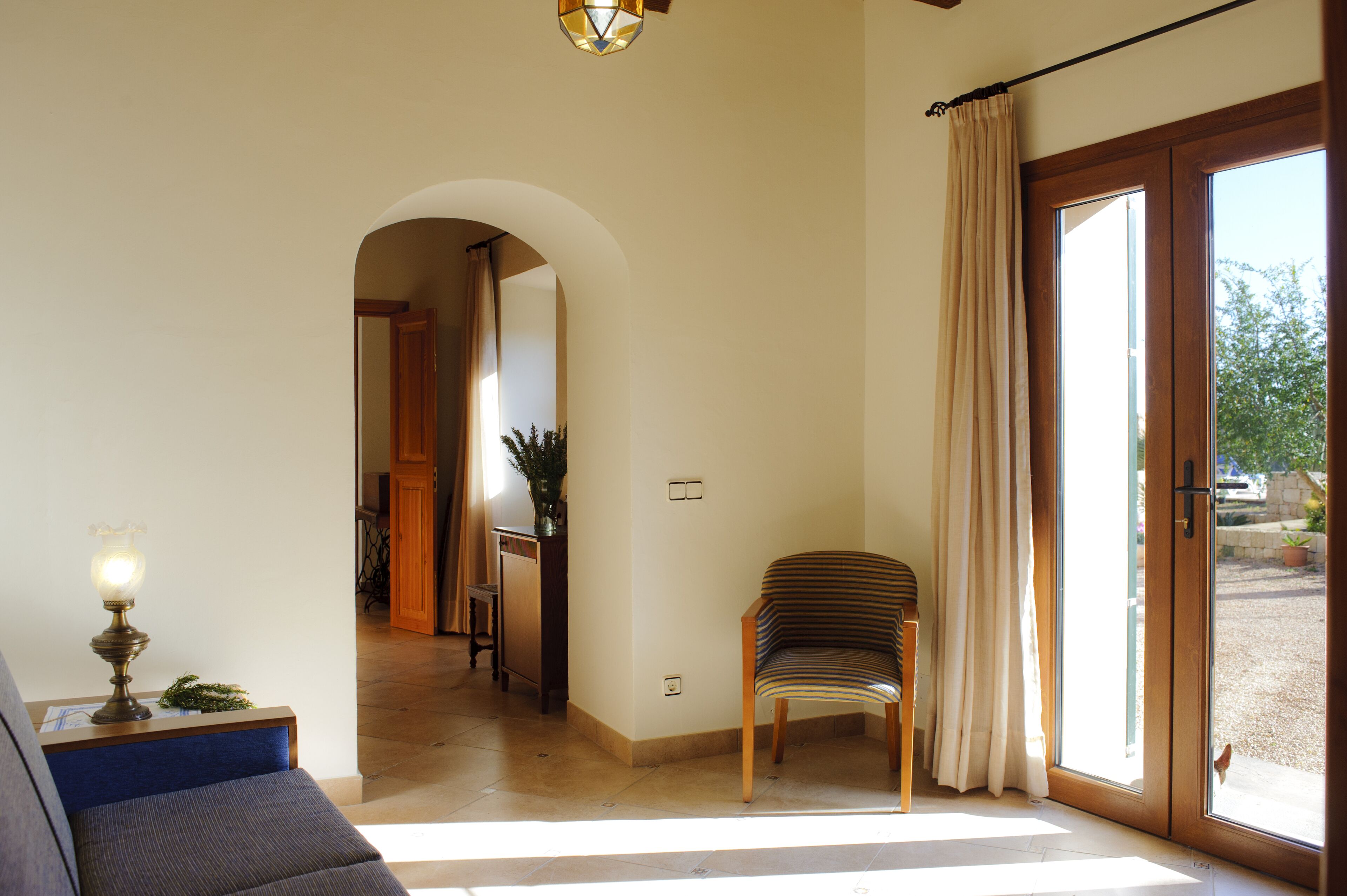 Una habitación con sofá, sillón, lámpara, puerta que da al exterior y una planta.