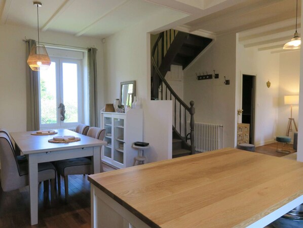 A dining area with a wooden table and chairs, a white cabinet, and a staircase leading to an upper floor.
