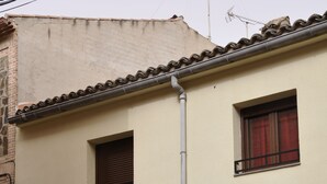 Ein zweistöckiges Gebäude mit einem Ziegeldach, mehreren Fenstern mit Metallgitter und einem sichtbaren Stromkasten an der Wand.