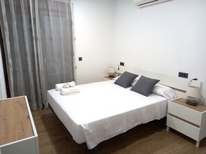 A neatly made bed with white linens and two pillows, a bedside table with a lamp, and a wooden nightstand. - COMPLETELY RENOVATED HOUSE WITH FREE WIFI (Toledo)
