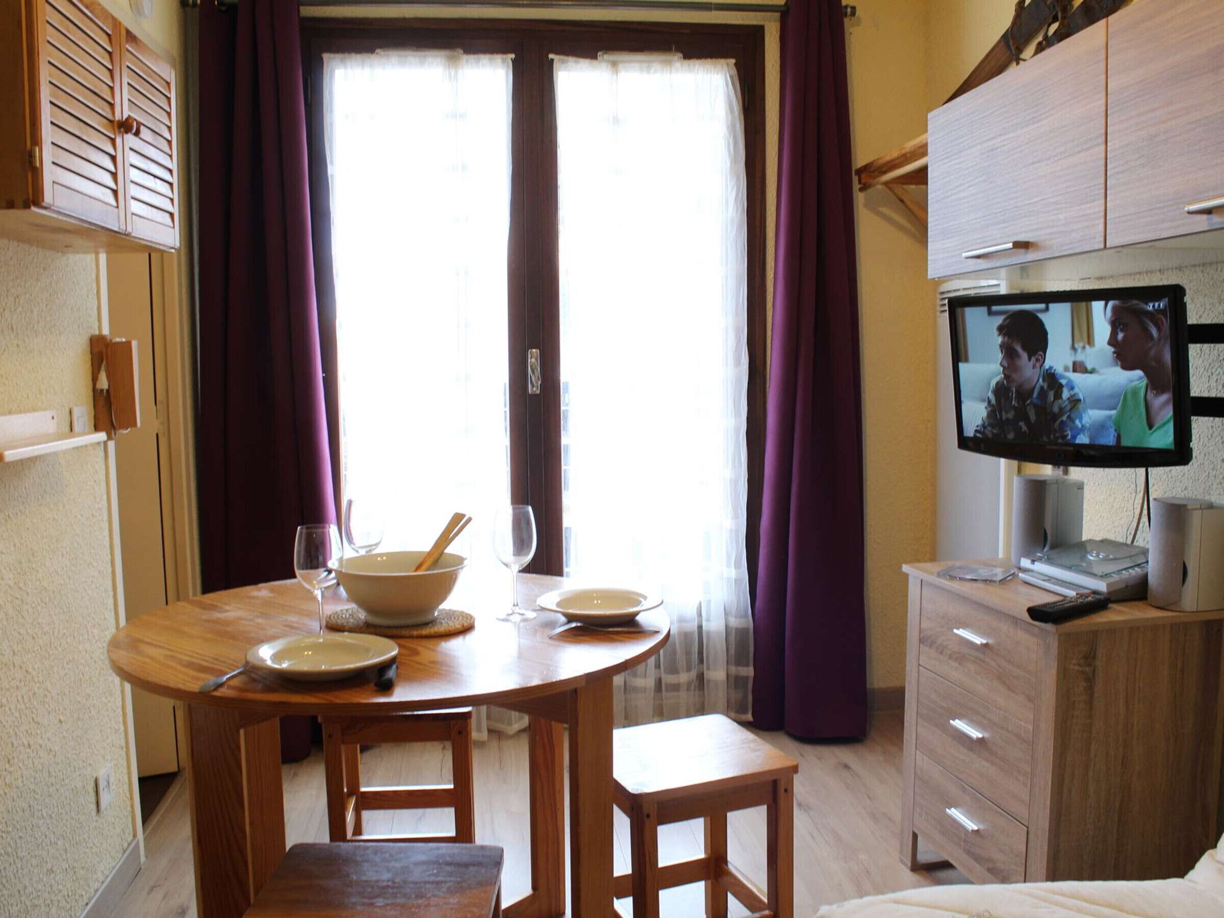 Zona pranzo con tavolo in legno, sedie e televisore su un mobiletto.