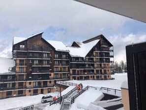Um edifício de vários andares com varandas, telhado coberto de neve e escadaria que leva à entrada.