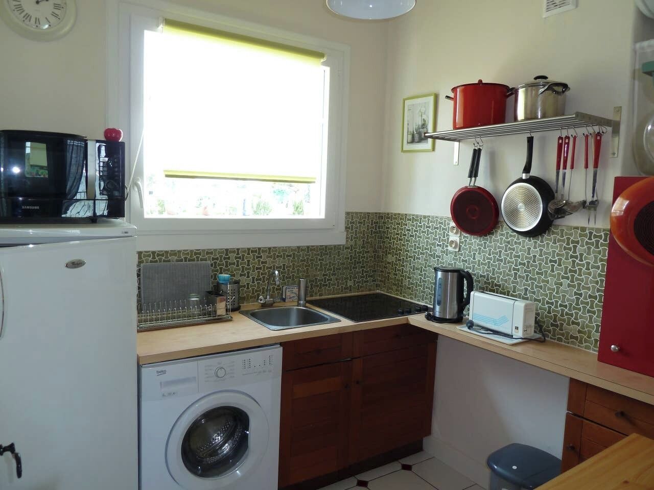 A compact kitchen with a washing machine, a sink, a microwave, and a window providing natural light.