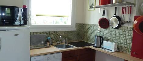 A compact kitchen with a washing machine, a sink, a microwave, and a window providing natural light.