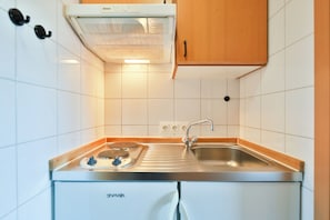 Une cuisine de taille réduite, équipée d’une cuisinière Bosch, d’un évier et de meubles de rangement en bois.