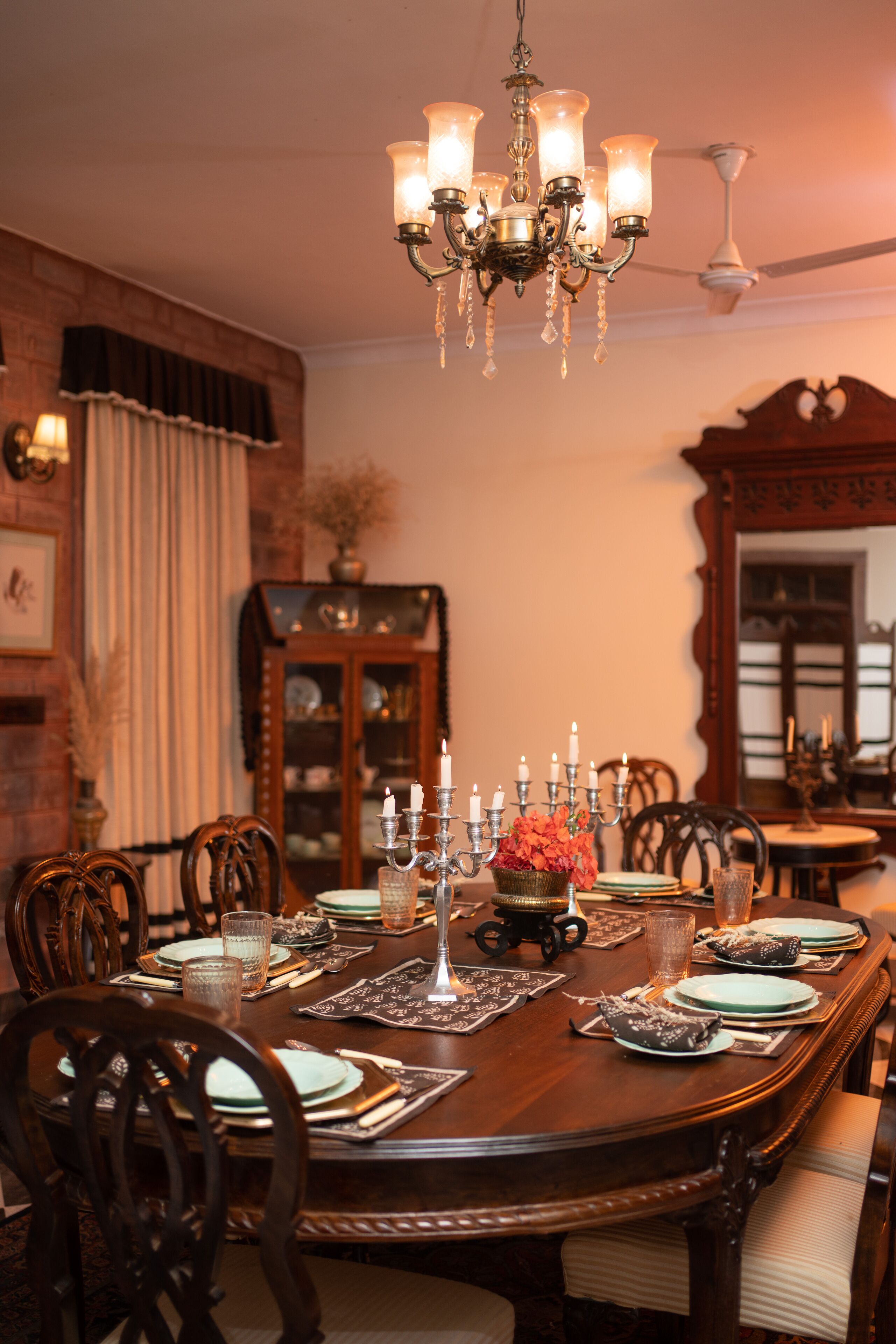 Comedor con mesa de madera lista para una comida, una araña y un espejo grande en la pared.