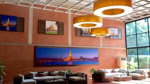 Un hall d’entrée spacieux, agrémenté d’un grand tableau représentant un paysage urbain, de plusieurs coins salon et d’un éclairage moderne suspendu au plafond.