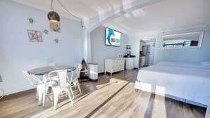 A modern hotel room with a wooden floor, a bed, a dining area with a table and chairs, a kitchenette, and a TV displaying 'Big Fish Rentals'. - Newly Remodeled Caravelle-Studio, Views with Pools (Myrtle Beach)