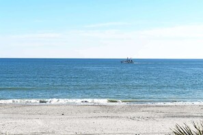 A beach with a boat in the distance and a clear sky.