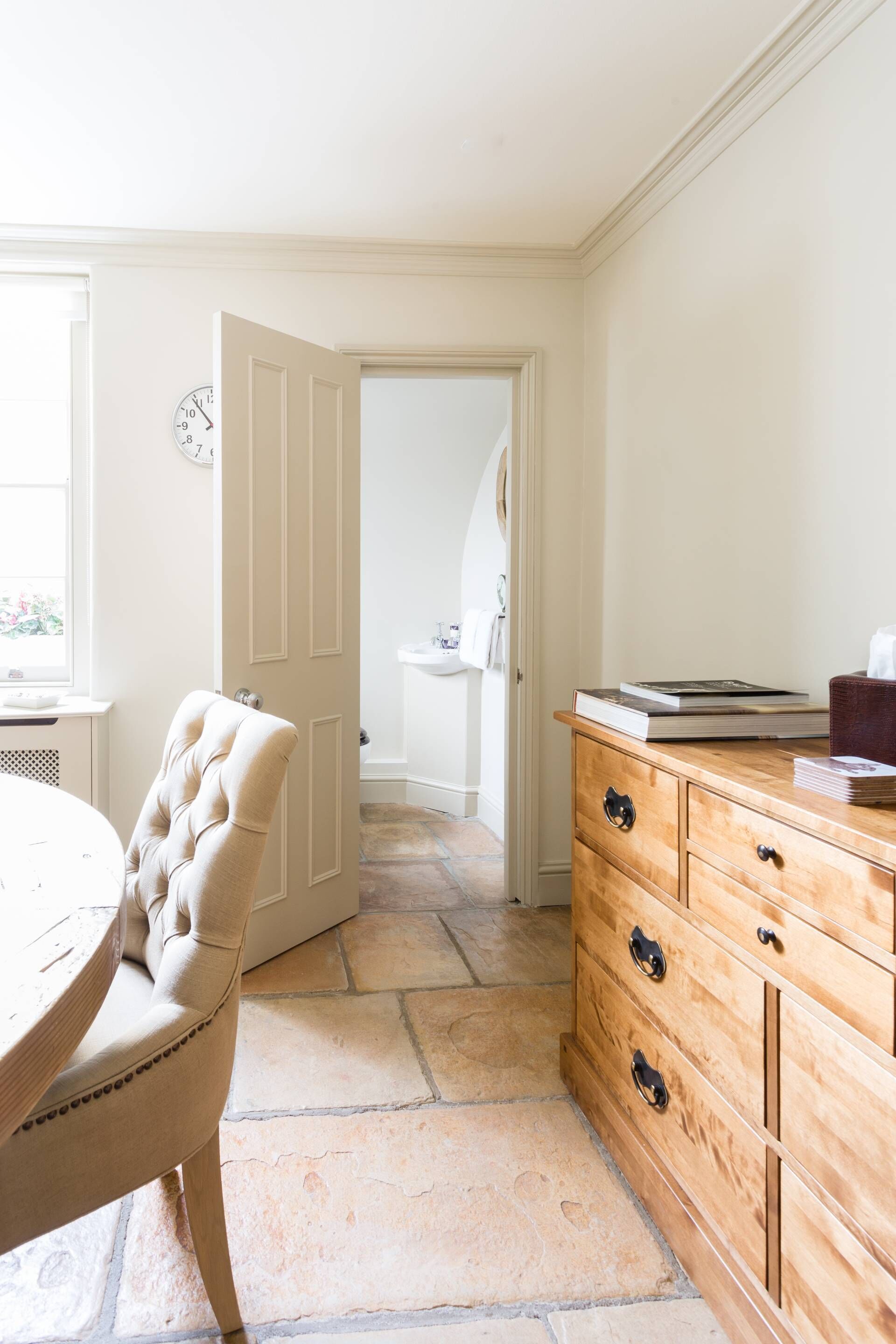 Une pièce avec un sol en pierre, une commode en bois dotée de tiroirs, une porte blanche et une chaise.