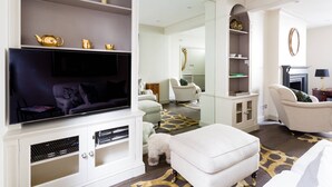 A modern living room with a flat-screen TV, white sofas, a patterned rug, and a dog.