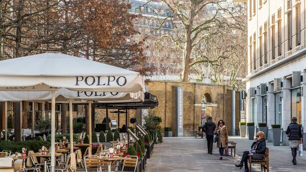 An outdoor café area with tables and chairs, a sign reading "POLPO", and a brick building in the background.