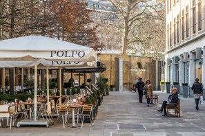 Un espace café en plein air avec des tables et des chaises, une enseigne indiquant « POLPO », et un bâtiment en briques en arrière-plan.