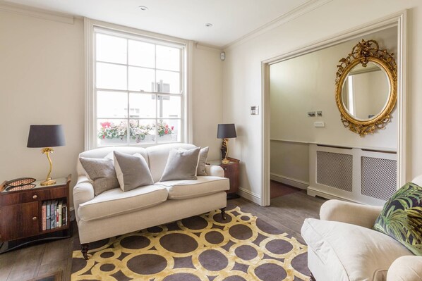 Une pièce bien éclairée, avec un canapé, un tapis à motifs, un fauteuil et un grand miroir doté d’un cadre orné.
