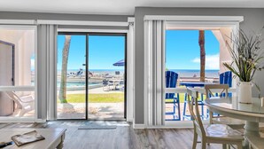 Une chambre moderne dotée d’une grande porte-fenêtre coulissante donnant sur une zone avec piscine, d’une table à manger avec des chaises et d’une vue sur la plage.