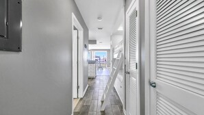 Un couloir avec un plancher en bois, des murs blancs et une porte fermée dotée de stores horizontaux.