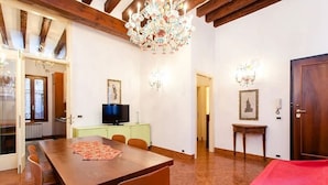 A dining area with a wooden table and chairs, a television on a cabinet, and a chandelier. - Signorile su Corte Veneziana (Venezia)