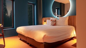 Een moderne slaapkamer met een groot bed, een ronde spiegel en een raam met gordijnen.