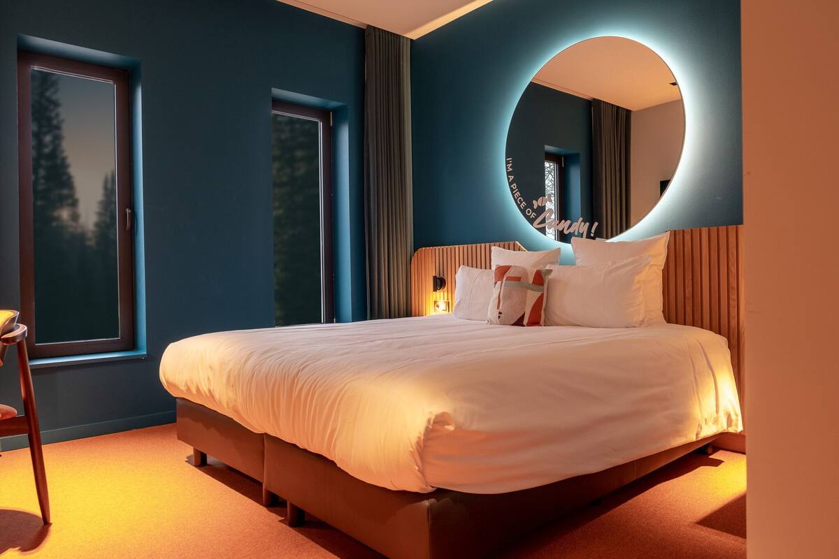 Un dormitorio moderno con una cama grande, un espejo circular y una ventana con cortinas.
