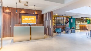 Een moderne receptie met een groot televisiescherm, houten lambrisering en een zithoek met stoelen en tafels.