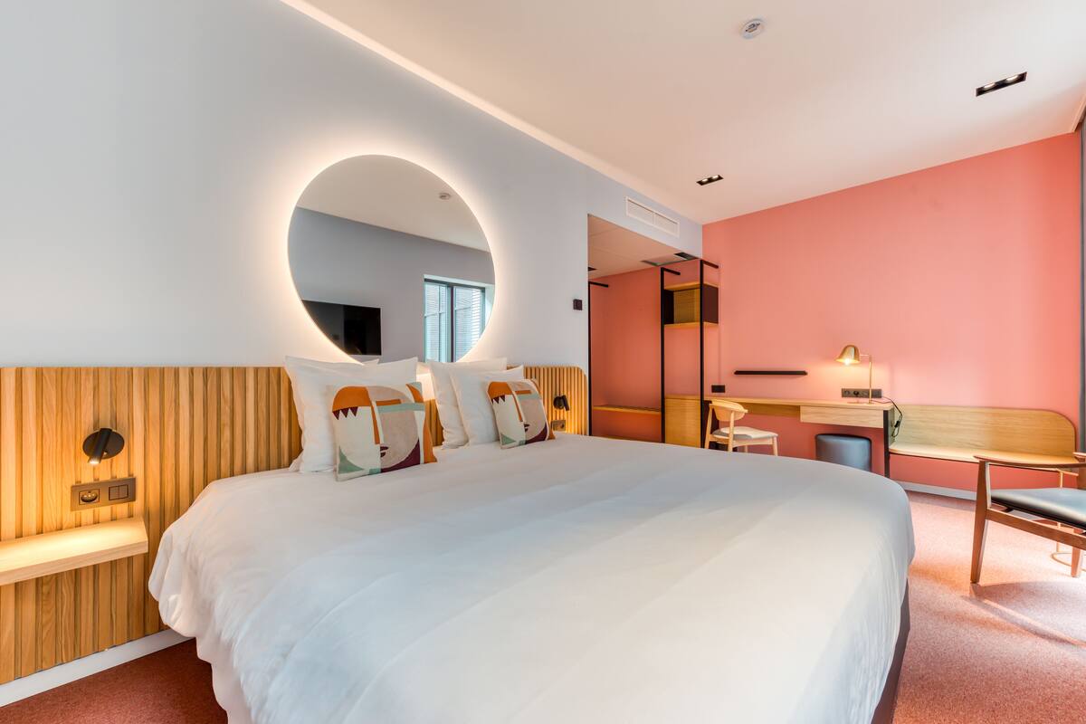 Una habitación de hotel moderna con una cama grande, un escritorio y un espejo circular.